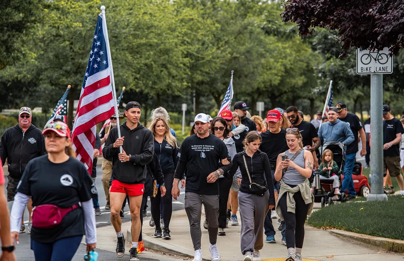 California community members walking together carrying American flags at a memorial event