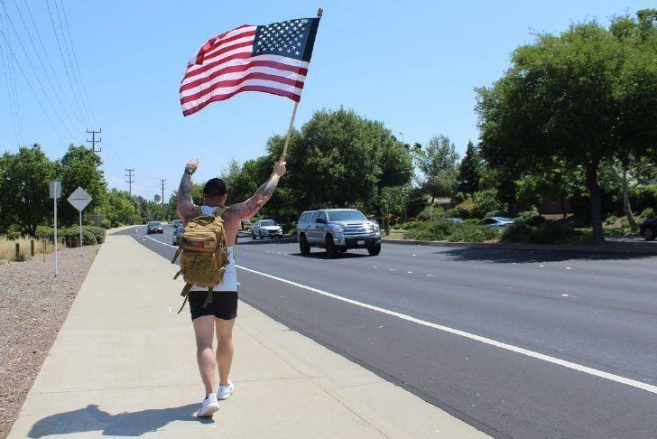 A veteran rucking along a California road carrying the American flag